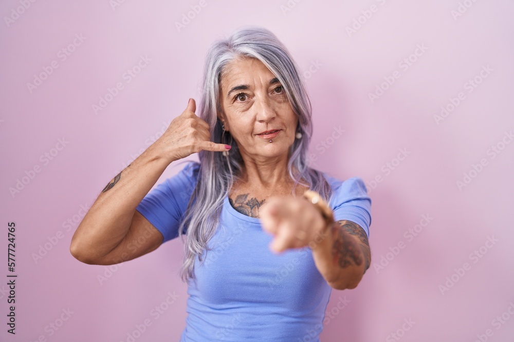 Middle age woman with tattoos standing over pink background smiling doing talking on the telephone gesture and pointing to you. call me.