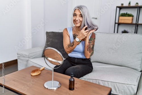 Middle age grey-haired woman having hair treatment sitting on sofa at home