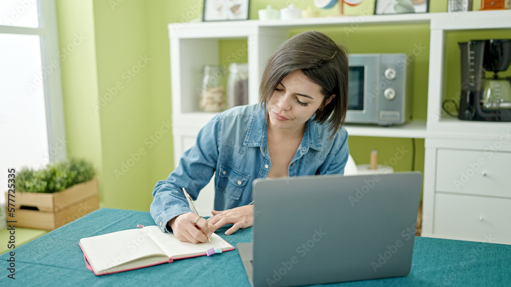 Young caucasian woman using laptop writing on notebook at home Young caucasian woman using laptop writing on notebook at home