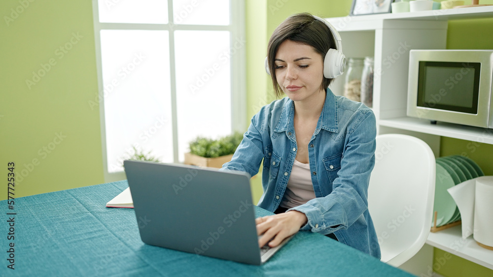 Young caucasian woman using laptop and headphones sitting on the table at home Young caucasian woman using laptop and headphones sitting on the table at home