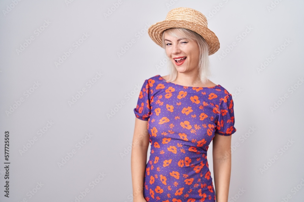 Young caucasian woman wearing flowers dress and summer hat winking looking at the camera with sexy expression, cheerful and happy face. Young caucasian woman wearing flowers dress and summer hat winking looking at the camera with sexy expression, cheerful and happy face.