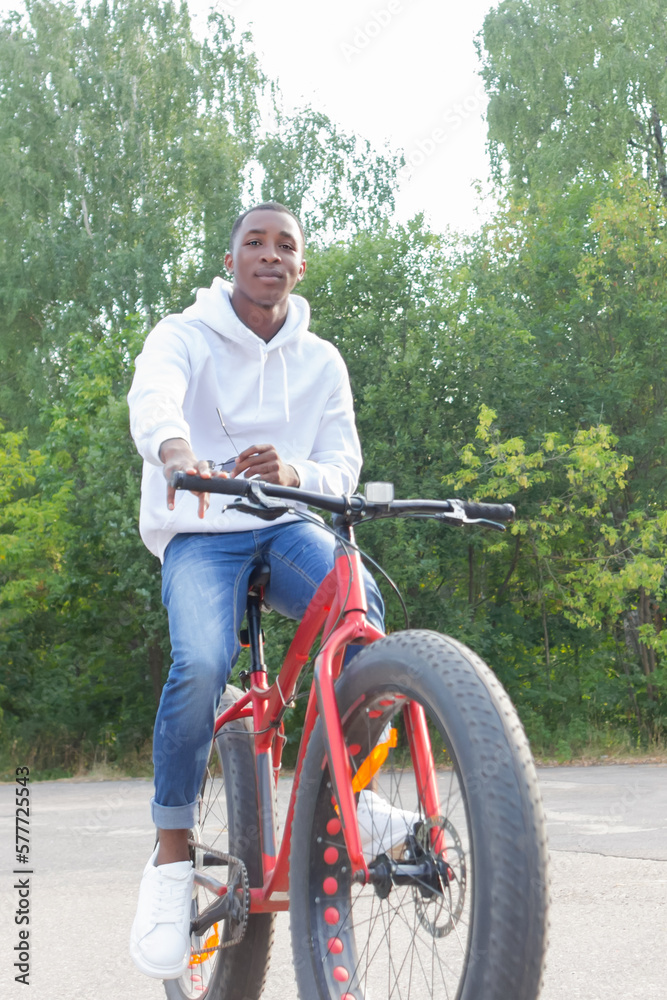 A happy African American man rides a bicycle through a public park. Portrait. Sports and recreation