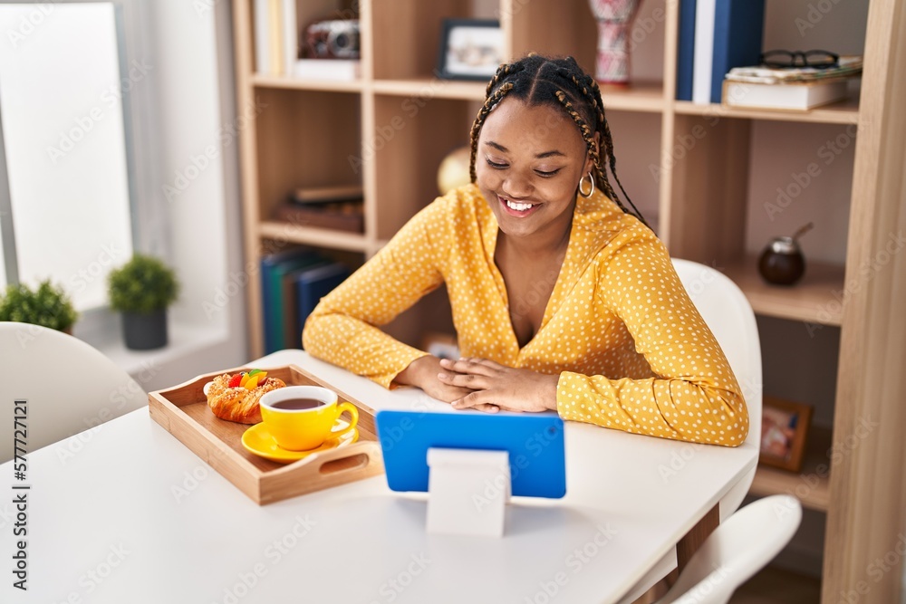African american woman having breakfast watching video on touchpad at home African american woman having breakfast watching video on touchpad at home