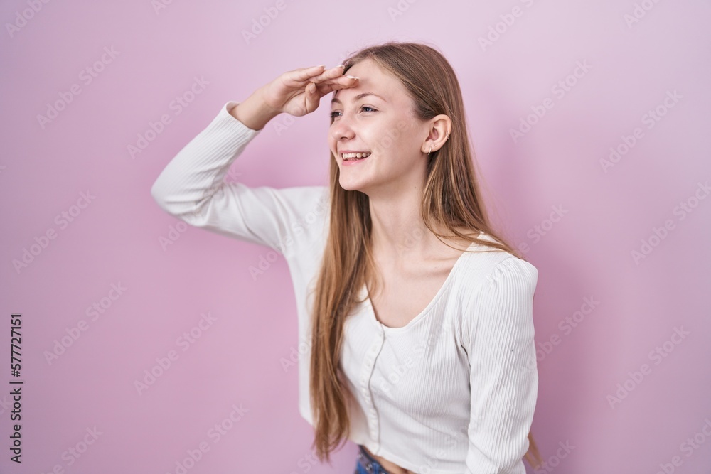 Young caucasian woman standing over pink background very happy and smiling looking far away with hand over head. searching concept.