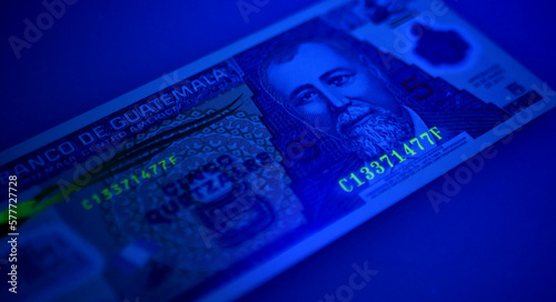 Guatemalan banknotes under UV light. Checking for counterfeit money. Close-up Guatemala quetzales. UV light banknote detector. Fake money testing