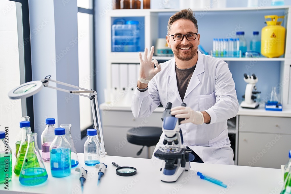 Middle age caucasian man working at scientist laboratory doing ok sign with fingers, smiling friendly gesturing excellent symbol Middle age caucasian man working at scientist laboratory doing ok sign with fingers, smiling friendly gesturing excellent symbol
