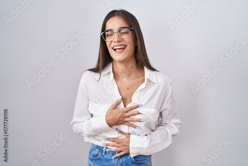 Young brunette woman wearing glasses smiling and laughing hard out loud because funny crazy joke with hands on body.
