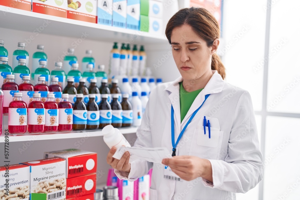 Young woman pharmacist holding pills bottle reading prescription at pharmacy