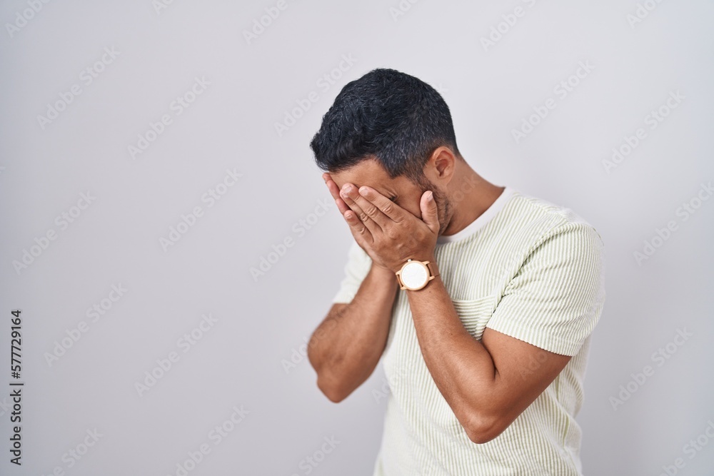 Hispanic man with beard standing over isolated background with sad expression covering face with hands while crying. depression concept. Hispanic man with beard standing over isolated background with sad expression covering face with hands while crying. depression concept.