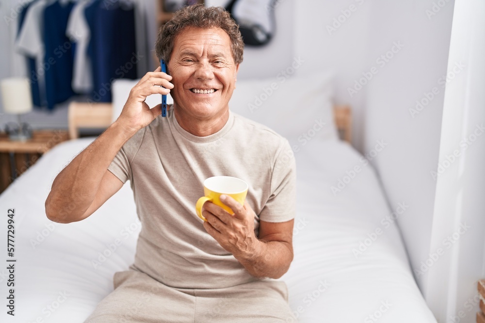 Middle age man talking on smartphone drinking coffee at bedroom Middle age man talking on smartphone drinking coffee at bedroom