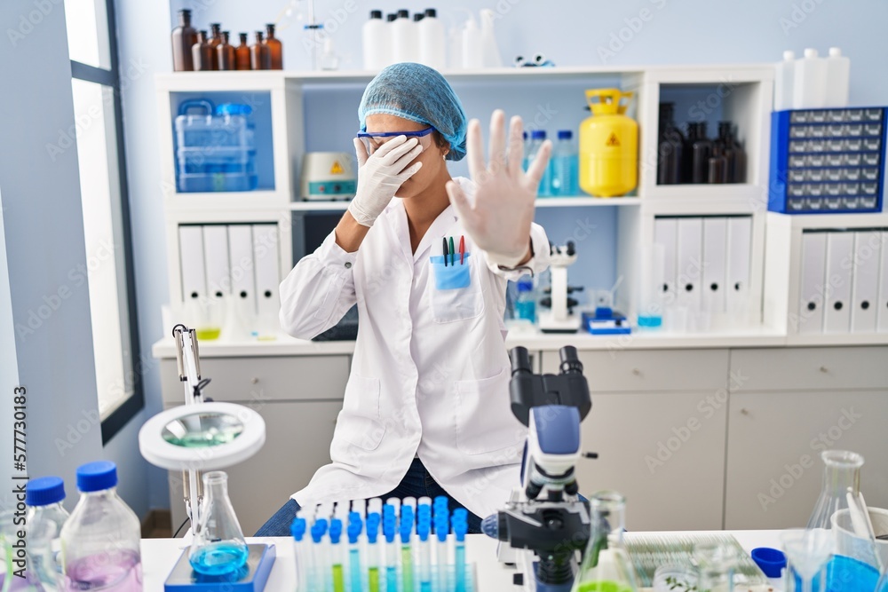 Brunette woman working at scientist laboratory covering eyes with hands and doing stop gesture with sad and fear expression. embarrassed and negative concept. Brunette woman working at scientist laboratory covering eyes with hands and doing stop gesture with sad and fear expression. embarrassed and negative concept.