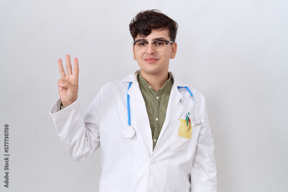 Young non binary man wearing doctor uniform and stethoscope showing and pointing up with fingers number three while smiling confident and happy. Young non binary man wearing doctor uniform and stethoscope showing and pointing up with fingers number three while smiling confident and happy.