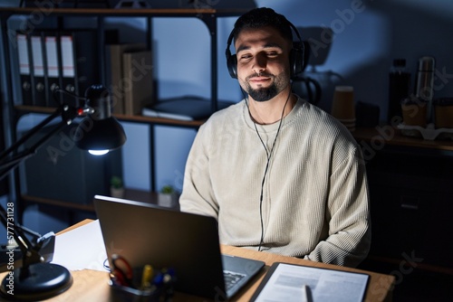 Young handsome man working using computer laptop at night smiling looking to the side and staring away thinking.