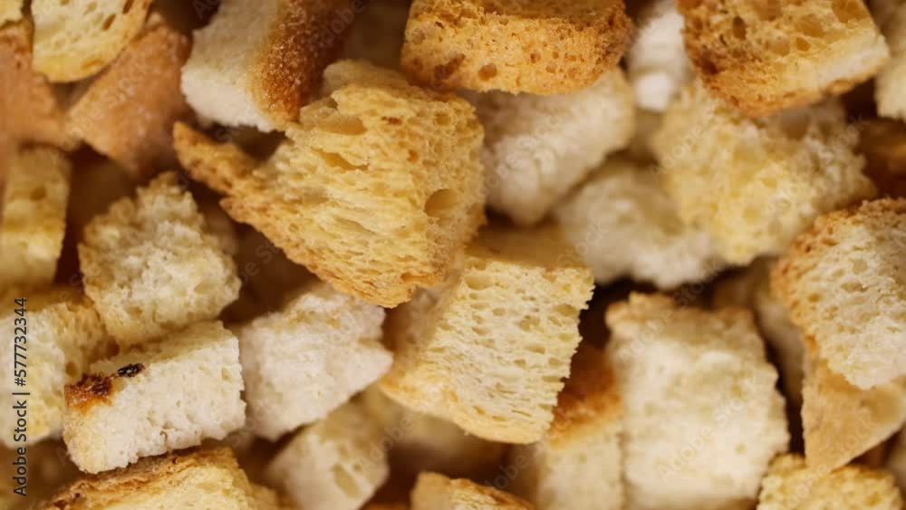 Crispy toasted bread falling down spinning in slow motion. Cubes of toasted bread close-up. Macro shot of bread crumbs. Crispy toasted bread falling down spinning in slow motion. Cubes of toasted bread close-up. Macro shot of bread crumbs.