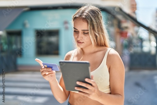 Young blonde woman using touchpad and credit card at street