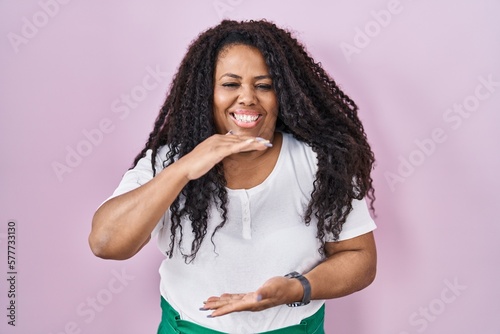 Plus size hispanic woman standing over pink background gesturing with hands showing big and large size sign, measure symbol. smiling looking at the camera. measuring concept.