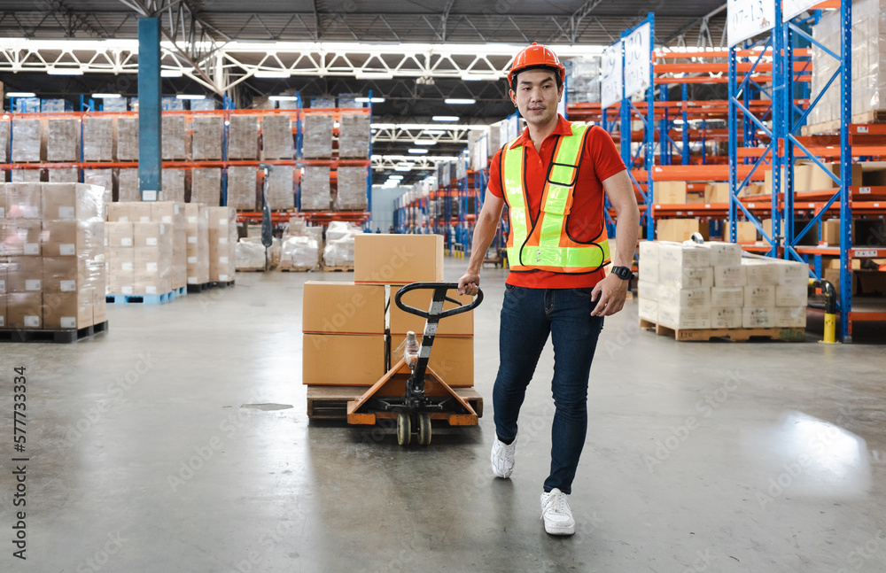 Young man pulling hand pallet truck loading package boxes stacked in