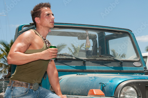 attractive athletic young man leaning on his car drinking beer