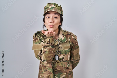 Young south asian woman wearing camouflage army uniform looking at the camera blowing a kiss with hand on air being lovely and sexy. love expression.