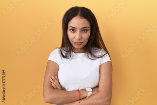 Young arab woman wearing casual white t shirt over yellow background skeptic and nervous, disapproving expression on face with crossed arms. negative person.