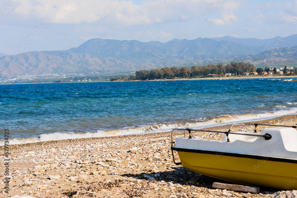 A lonely yellow boat stands on the rocky shore of the Mediterranean blue sea. Travel mood on a sunny day