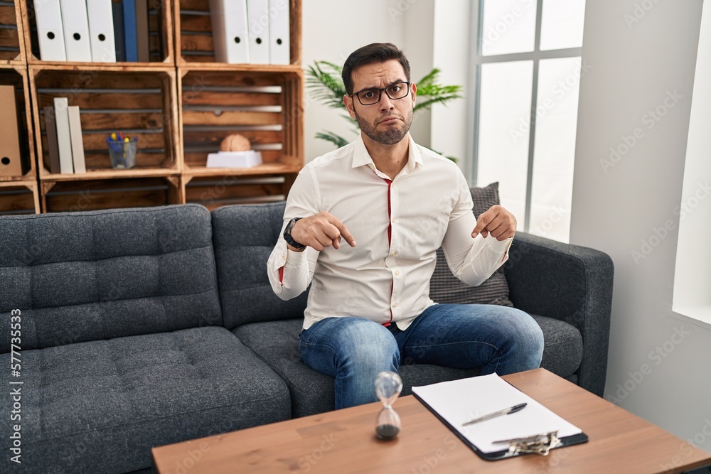 Young hispanic man with beard working at consultation office pointing down looking sad and upset, indicating direction with fingers, unhappy and depressed. Young hispanic man with beard working at consultation office pointing down looking sad and upset, indicating direction with fingers, unhappy and depressed.
