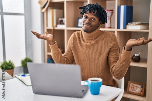 Valokuva Young african man with dreadlocks working using computer laptop clueless and confused expression with arms and hands raised