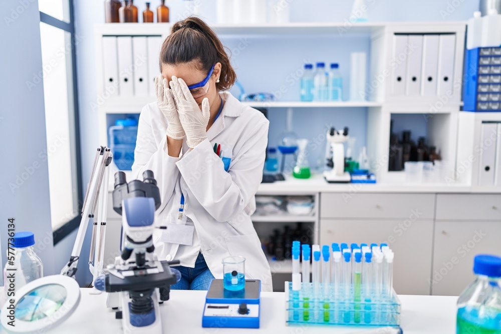 Fototapeta premium Young hispanic woman working at scientist laboratory with sad expression covering face with hands while crying. depression concept.