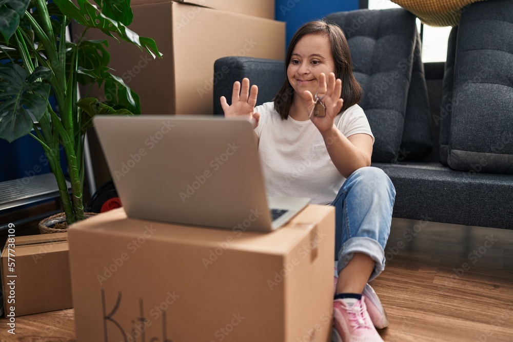 Hispanic girl with down syndrome sitting on the floor at new home with laptop looking positive and happy standing and smiling with a confident smile showing teeth Hispanic girl with down syndrome sitting on the floor at new home with laptop looking positive and happy standing and smiling with a confident smile showing teeth