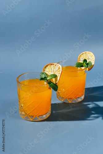 orange cocktail with mint and orange chips on a blue background