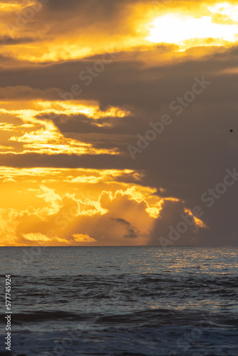 Dark sea at sunset and sun breaking through dark gray clouds