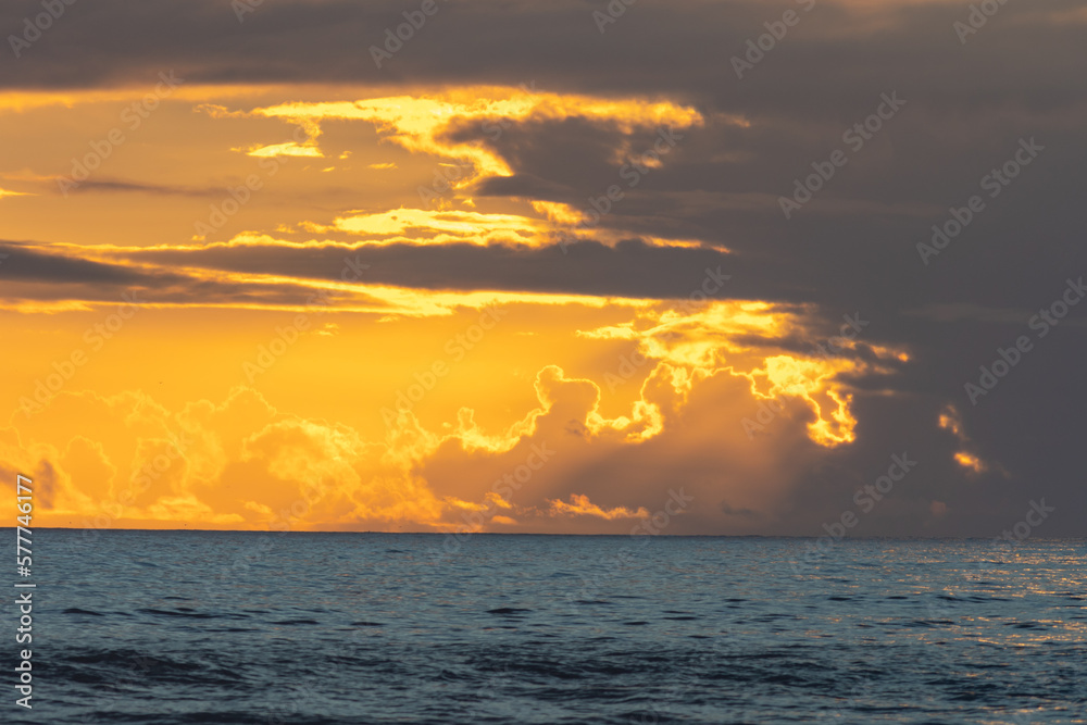 A sea at sunset and sun breaking through dark gray clouds