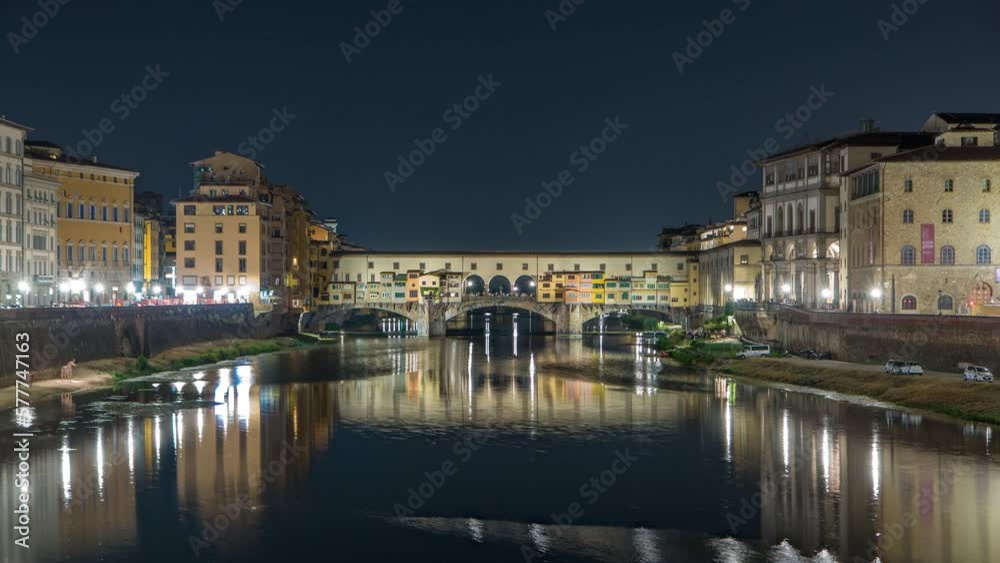 Famous Ponte Vecchio bridge timelapse over the Arno river in Florence, Italy, lit up at night. Reflection on water. Illuminated old houses on the side