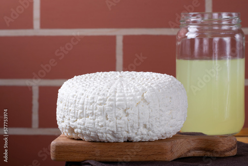 Fresh homemade cheese served on wooden board and jar of whey against the brick wall. Copy space photo