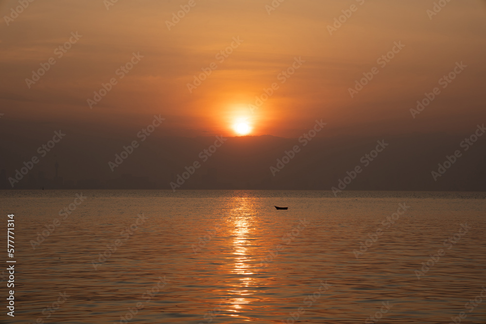 Calm sea with sunset and boat in the distance. Meditation on the background of the ocean. Calm seascape, city skyline in the distance, Thailand