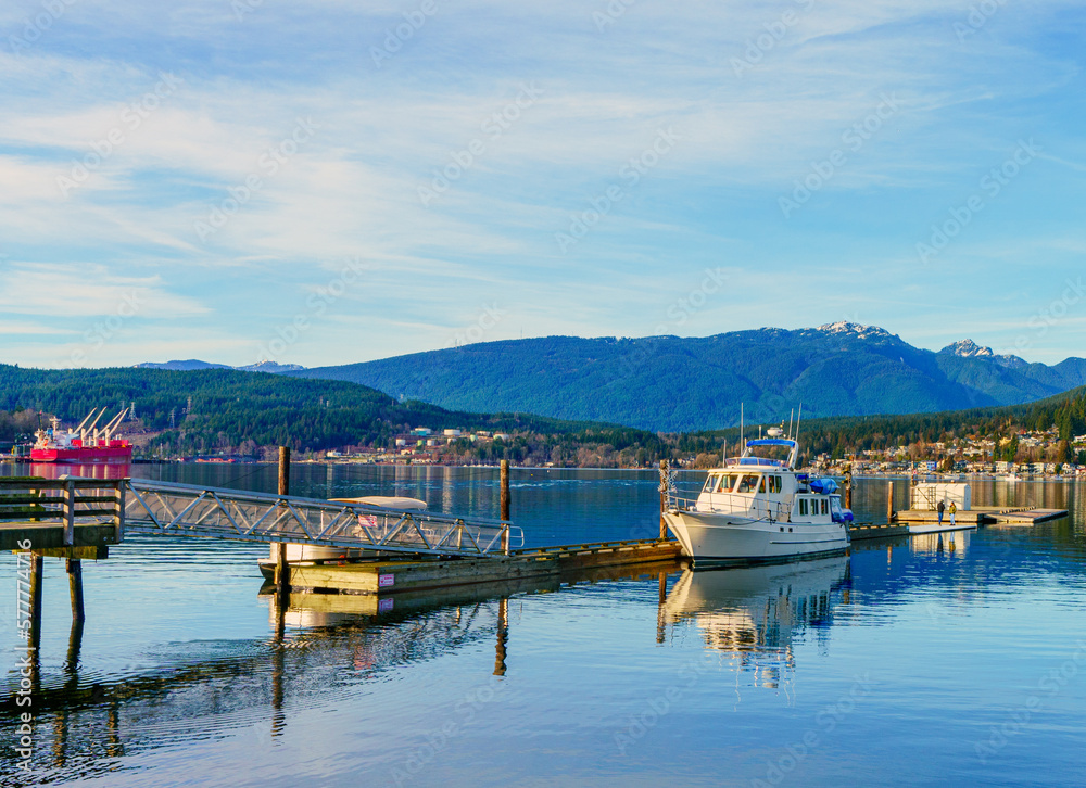 Fototapeta premium Cabin cruiser moored at Rocky Point Park, Port Moody, BC on pristine Burrard Inlet, with oil tanker and refinery in background.
