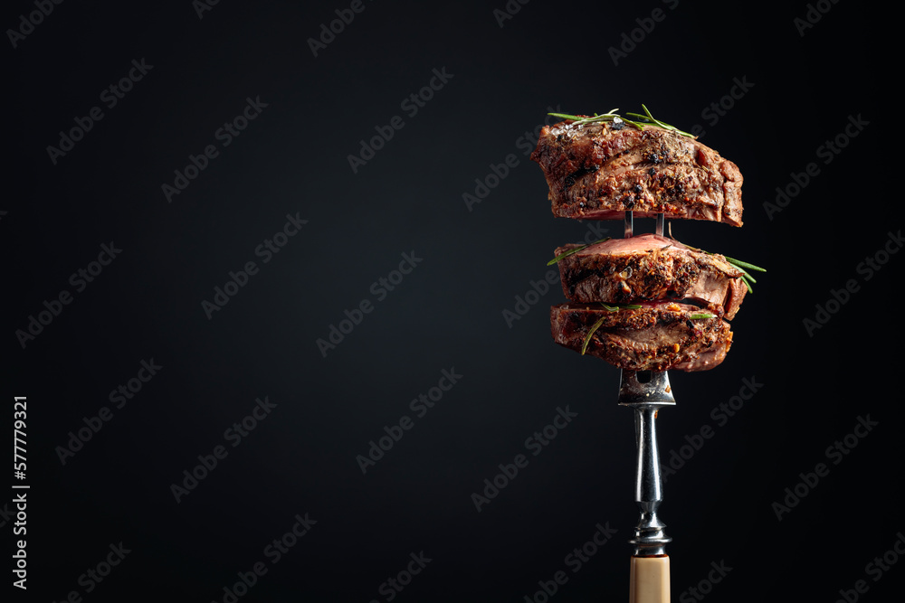 Medium rare beef steak with rosemary on a black background.