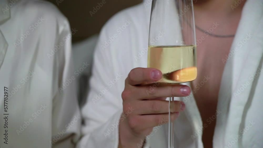 Man and woman clink glasses with champagne sparkling wine. Young couple in underwear and bathrobes in bedroom. Morning of bride groom on wedding day. Husband and wife love, romantic weekend, honeymoon Man and woman clink glasses with champagne sparkling wine. Young couple in underwear and bathrobes in bedroom. Morning of bride groom on wedding day. Husband and wife love, romantic weekend, honeymoon
