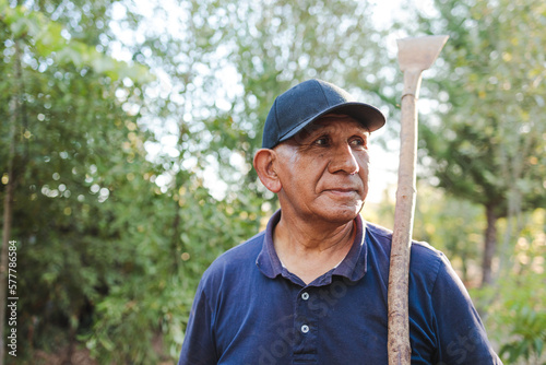 Close up portrait of an elderly indigenous latin field worker man holding a garden scraper.