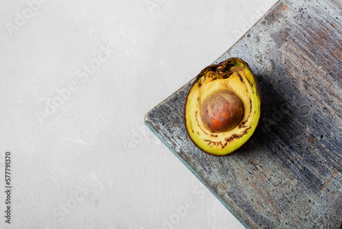 Rotten avocado, overriped, bad avocado on cutting board. Half sliced fruit, freegan food concept, grey background. The theme of careful consumption and care for the environment. Copyspace