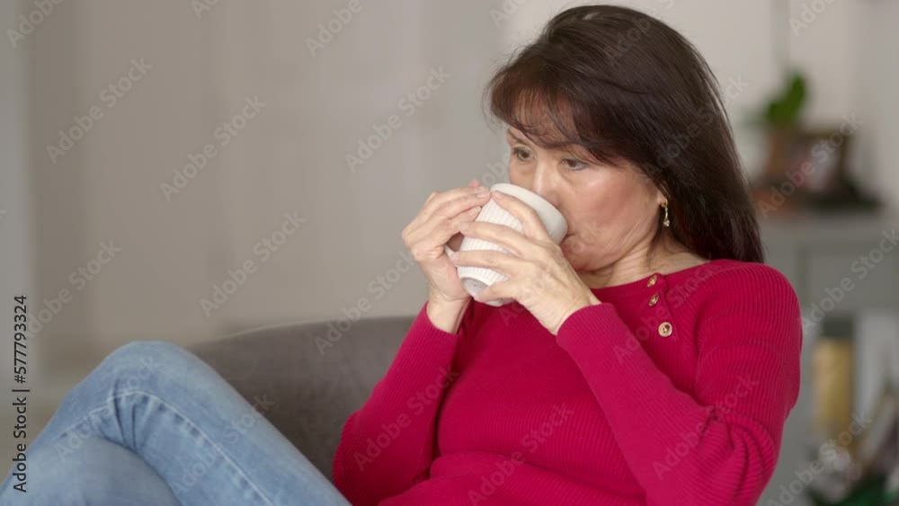 Attractive stylish woman long hair wearing red top, denim jeans smiling enjoying drinking coffee brushing hair from face relaxing, legs resting up on living room chair. Beautiful asian female is happy Attractive stylish woman long hair wearing red top, denim jeans smiling enjoying drinking coffee brushing hair from face relaxing, legs resting up on living room chair. Beautiful asian female is happy
