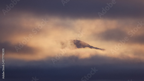 atardecer paisaje nevado, colina en invierno, con bruma y nubes bajas, picos de montañas rodeadas de nubes 