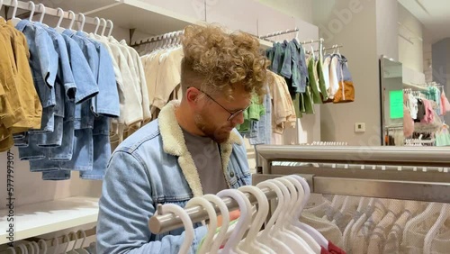 Man with glasses chooses gift clothes for small child in clothing store. Inflates the choice of clothes for children. The concept of caring loving father, uncle, brother relative
