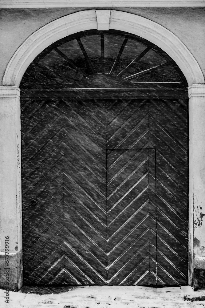 Black wooden vintage arch doors during heavy snow fall. Vertical photo
