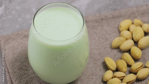 Organic non dairy pistachio milk in glass with pistachionuts on gray background. Vegan plant based milk. Tilt down photo