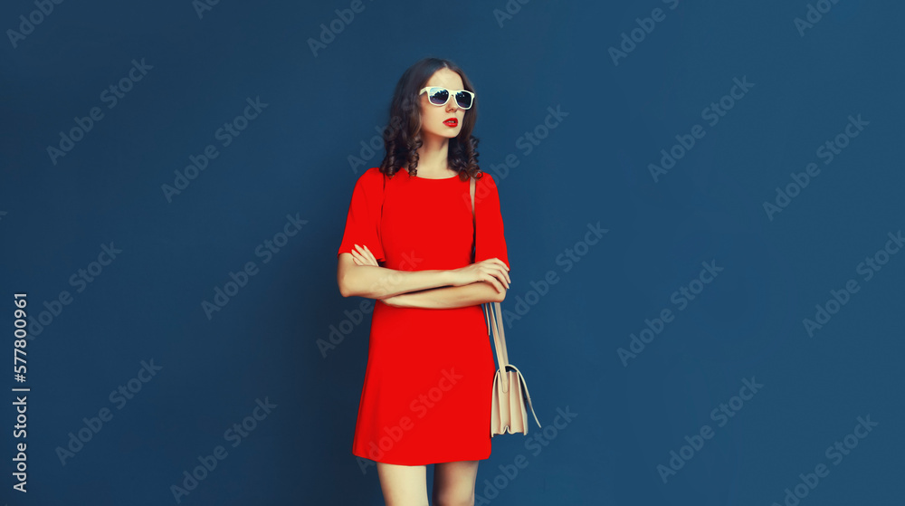 Portrait of beautiful young woman in red dress with handbag on blue background