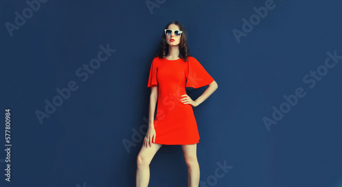 Portrait of beautiful young woman posing in red dress on blue background