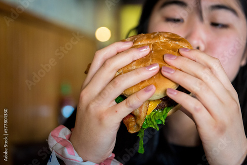 Young asian girl holding bacon cheese hamburger