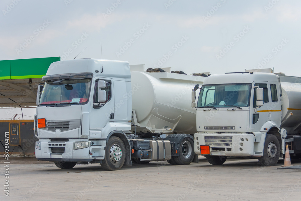 Two fuel trucks delivering fuel to the city fuel station parking.