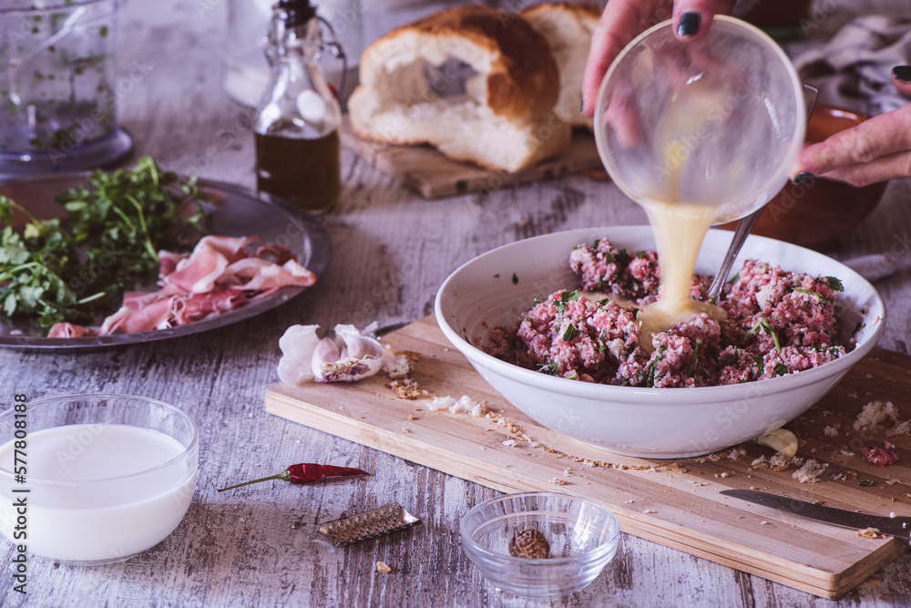 Adding egg to a meatball mix of beef, parmesan and parsley, on a wooden kitchen table Adding egg to a meatball mix of beef, parmesan and parsley, on a wooden kitchen table